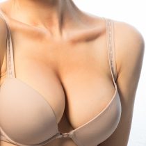 A woman with a breast lift and implants wears a nude colored bra.