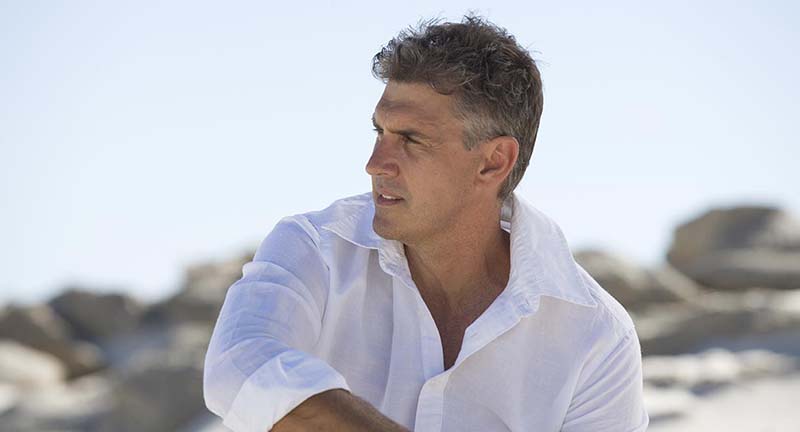 A handsome man sits outdoors after his neck lift.