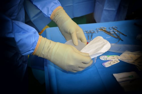 surgeon holding breast implant above tray